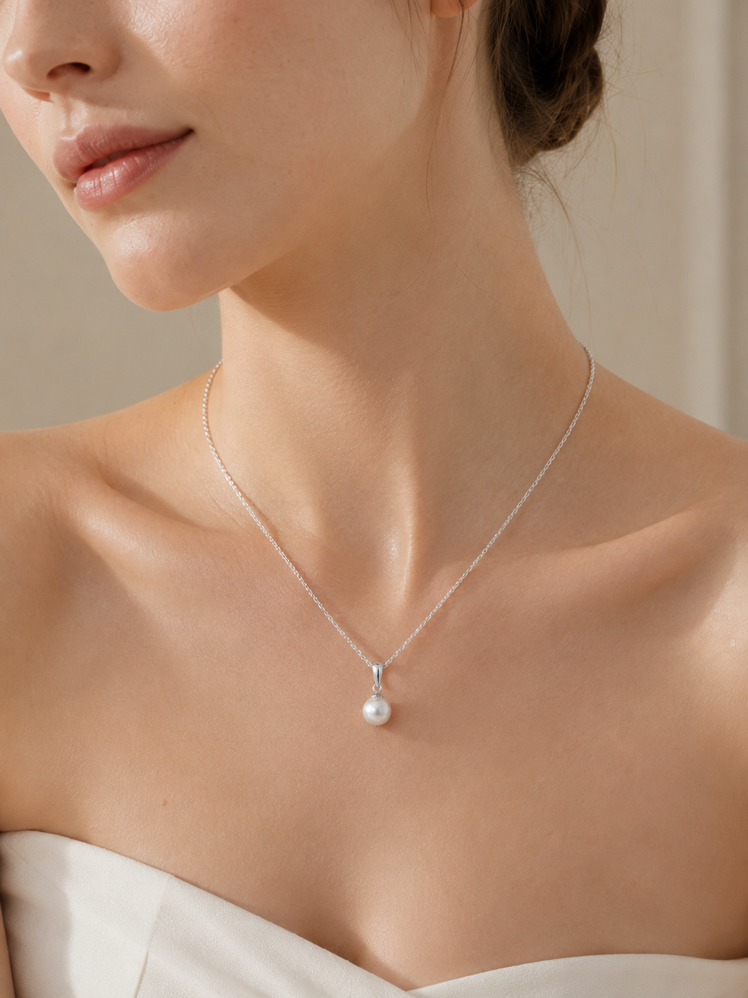 Model wearing a white freshwater pearl pendant on a fine silver-tone chain with an ivory neckline.