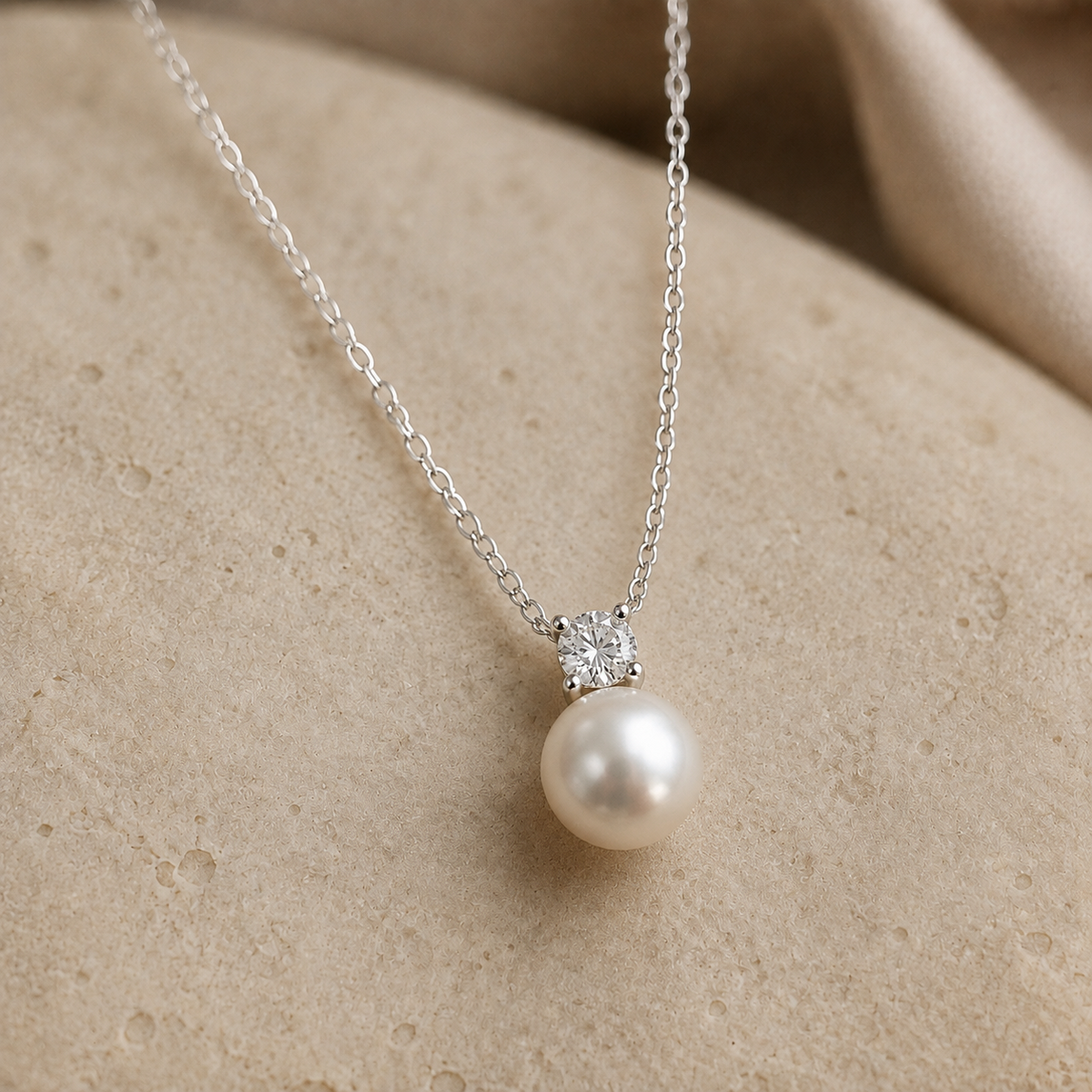Four-prong cubic zirconia above a round freshwater pearl on a sterling silver necklace, shown on ivory stone.