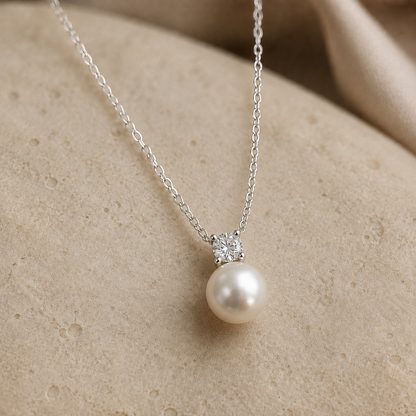 Four-prong cubic zirconia above a round freshwater pearl on a sterling silver necklace, shown on ivory stone.