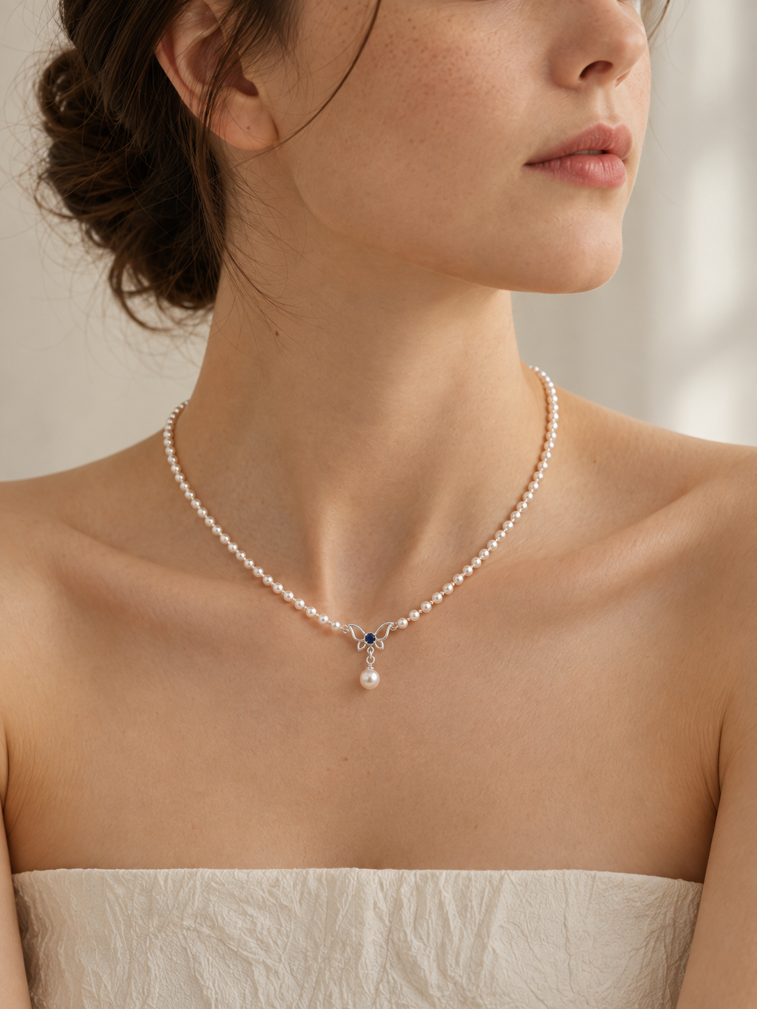 Close-up of small round freshwater pearls with a silver butterfly, blue zircon center and single pearl drop worn at the collarbone