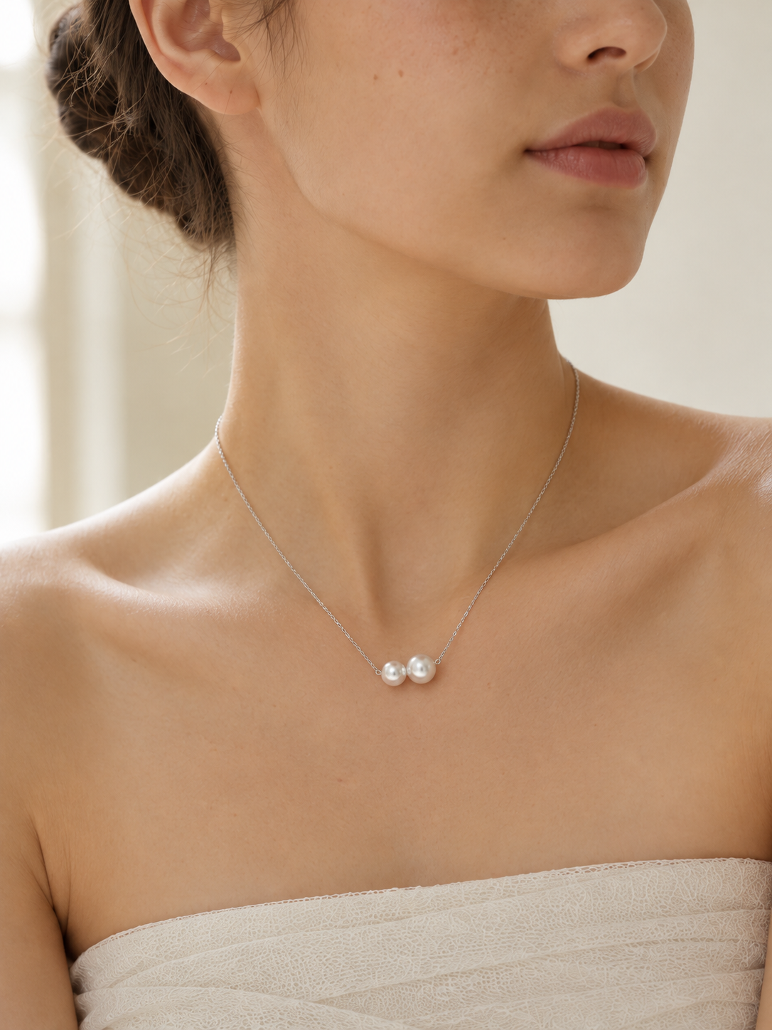 Close-up of two white freshwater pearls on a delicate silver necklace worn at the collarbone