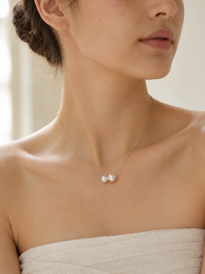 Close-up of two white freshwater pearls on a delicate silver necklace worn at the collarbone