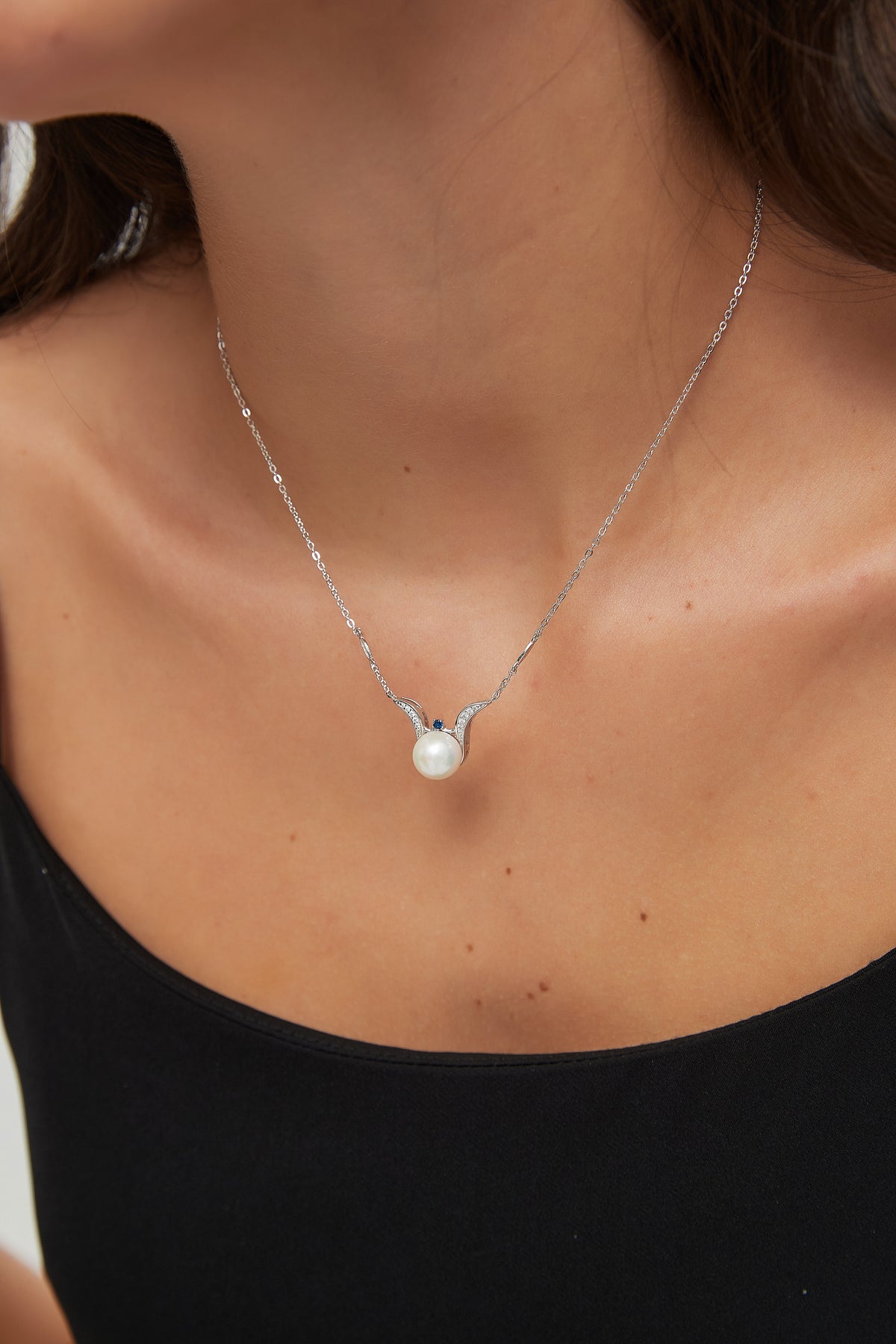 Sea Angel freshwater pearl necklace resting at the neckline, showing the round pearl, blue accent and sweeping silver curves.