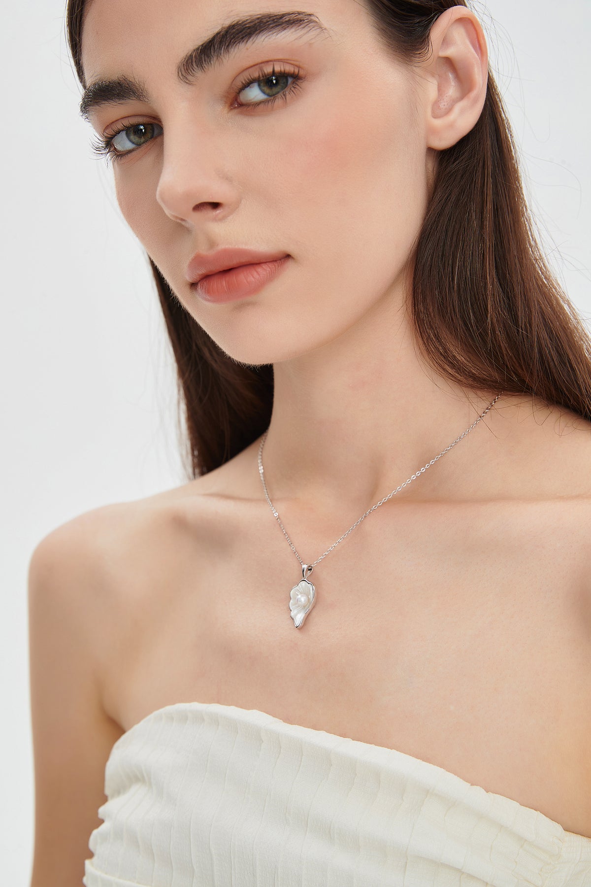 Model wearing the Sea Petal mother-of-pearl and freshwater pearl pendant necklace in sterling silver with an ivory strapless top.