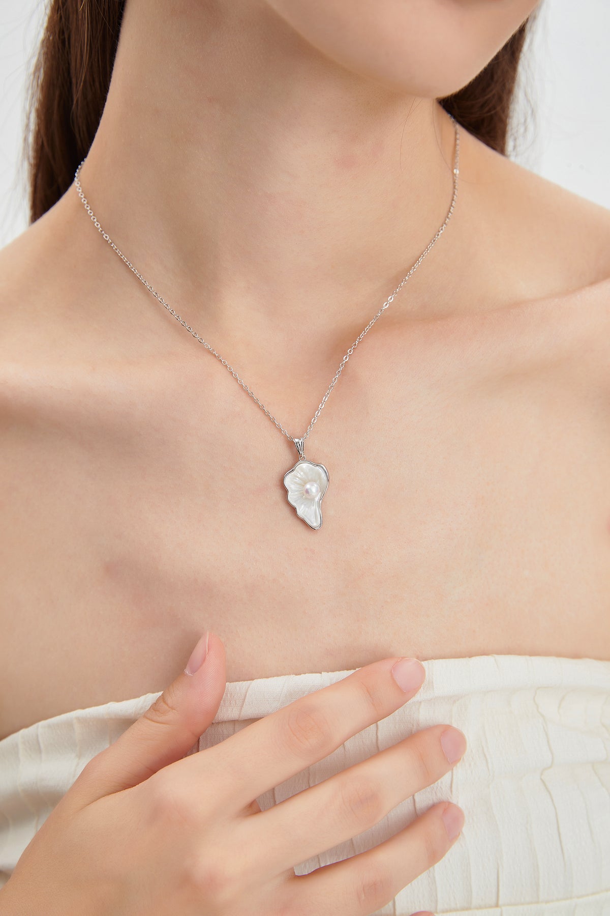 Sea Petal mother-of-pearl pendant necklace with a freshwater pearl and sterling silver chain, worn close to the neckline.