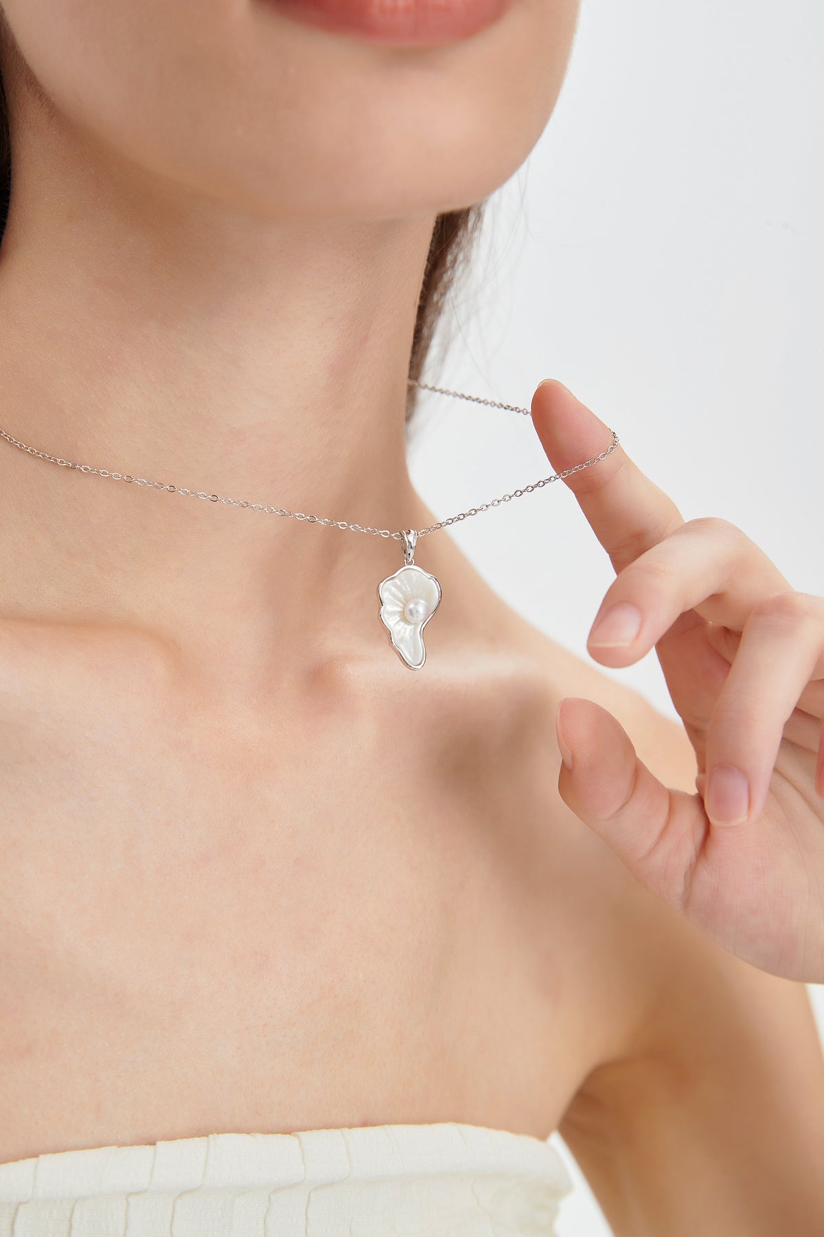 Close-up of the Sea Petal mother-of-pearl pendant and round freshwater pearl, with the sterling silver chain held by a model.