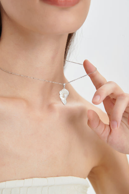Close-up of the Sea Petal mother-of-pearl pendant and round freshwater pearl, with the sterling silver chain held by a model.