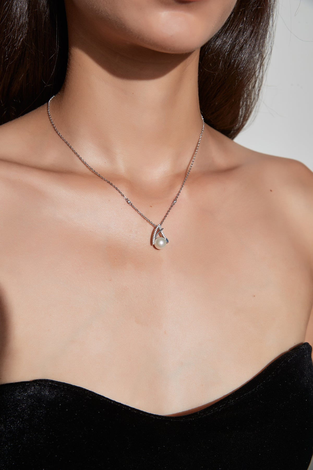 Sea Wish freshwater pearl pendant necklace resting at the neckline, with a round white pearl framed by slender silver curves.