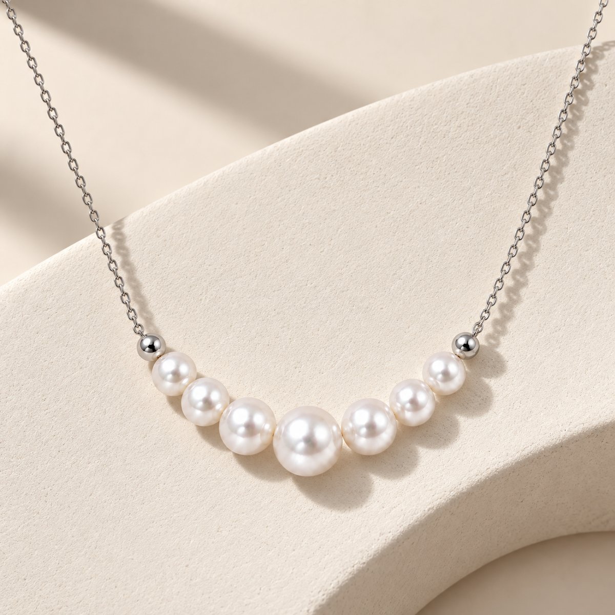 Silver freshwater pearl necklace arranged on an ivory sculptural surface with soft editorial lighting